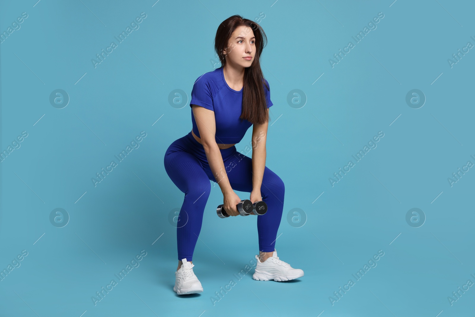 Photo of Woman in sportswear exercising with dumbbells on light blue background