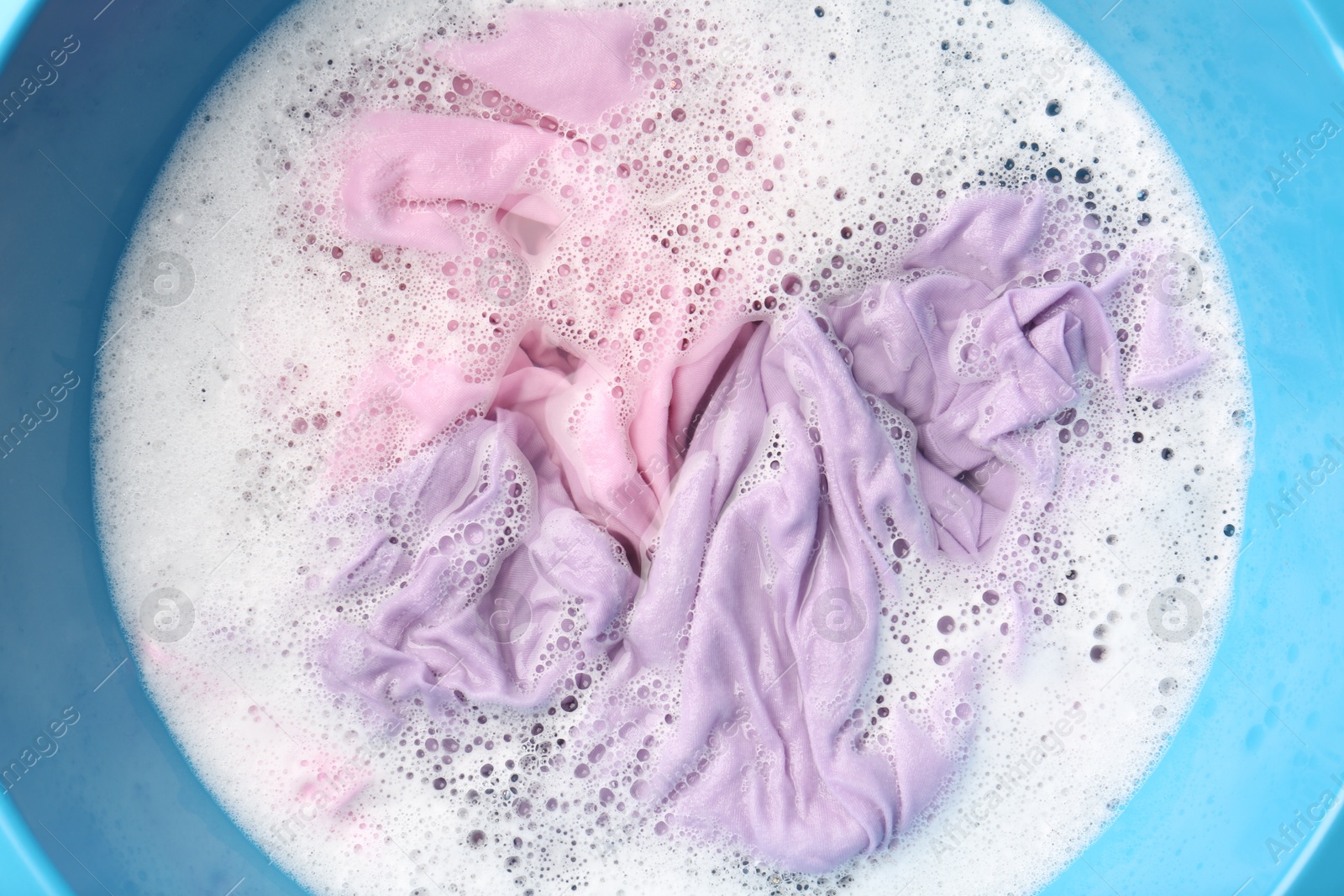 Photo of Colorful clothes soaked in water before washing, top view