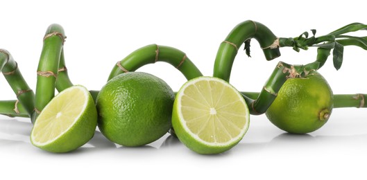 Photo of Fresh limes and bamboo stems on mirror surface against white background