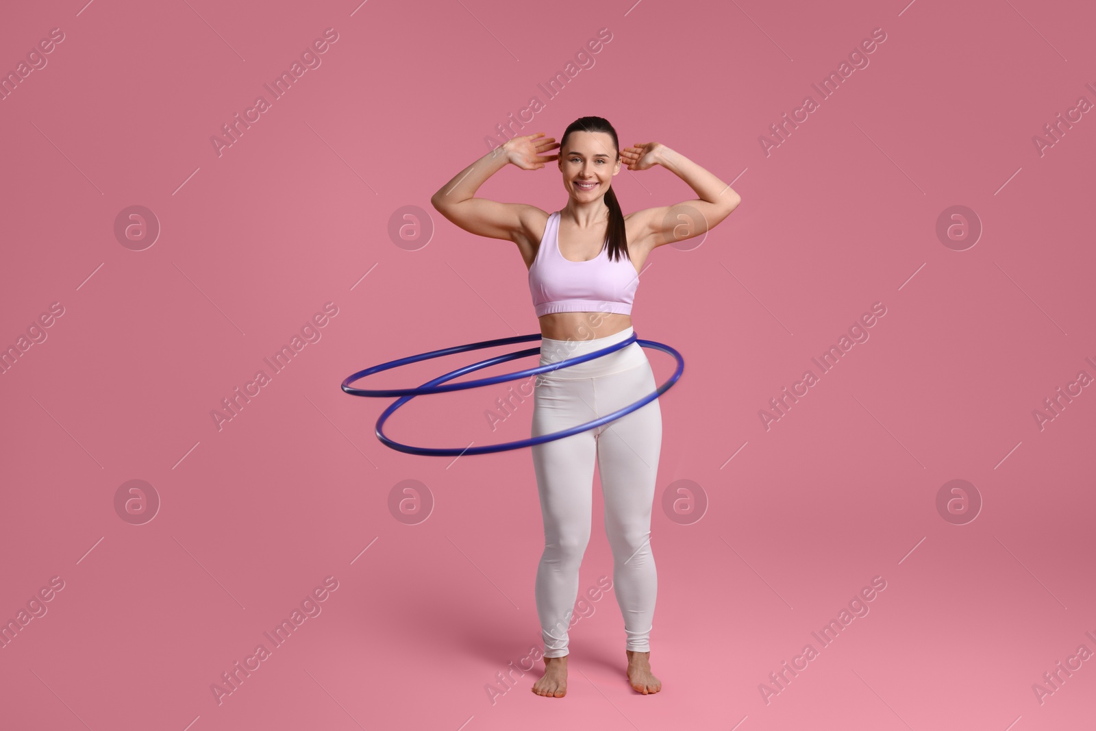 Photo of Smiling woman training with hula hoops on pink background