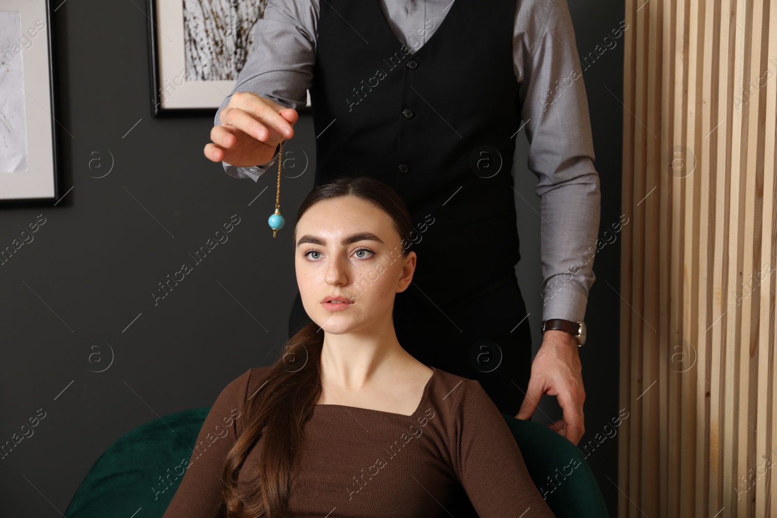 Photo of Psychologist using pendulum while working with patient during hypnosis session indoors, closeup