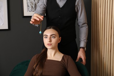 Photo of Psychologist using pendulum while working with patient during hypnosis session indoors, closeup