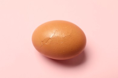 Photo of One egg with cracked shell on pink background, closeup