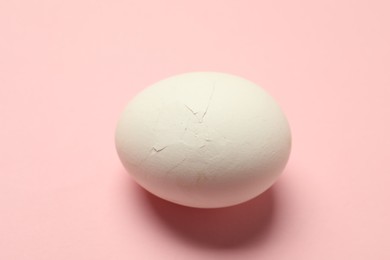 One egg with cracked shell on pink background, closeup