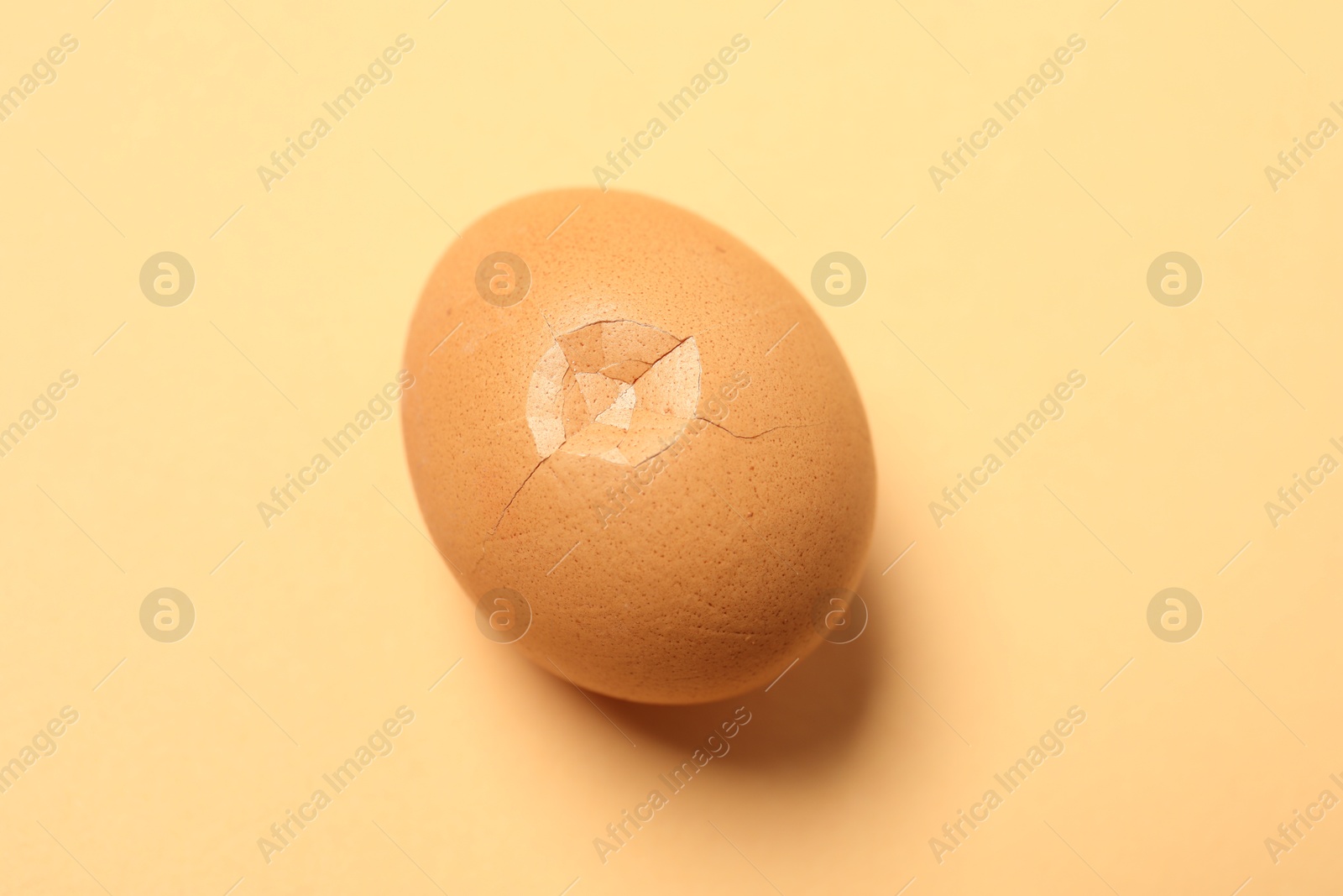 Photo of One egg with cracked shell on beige background