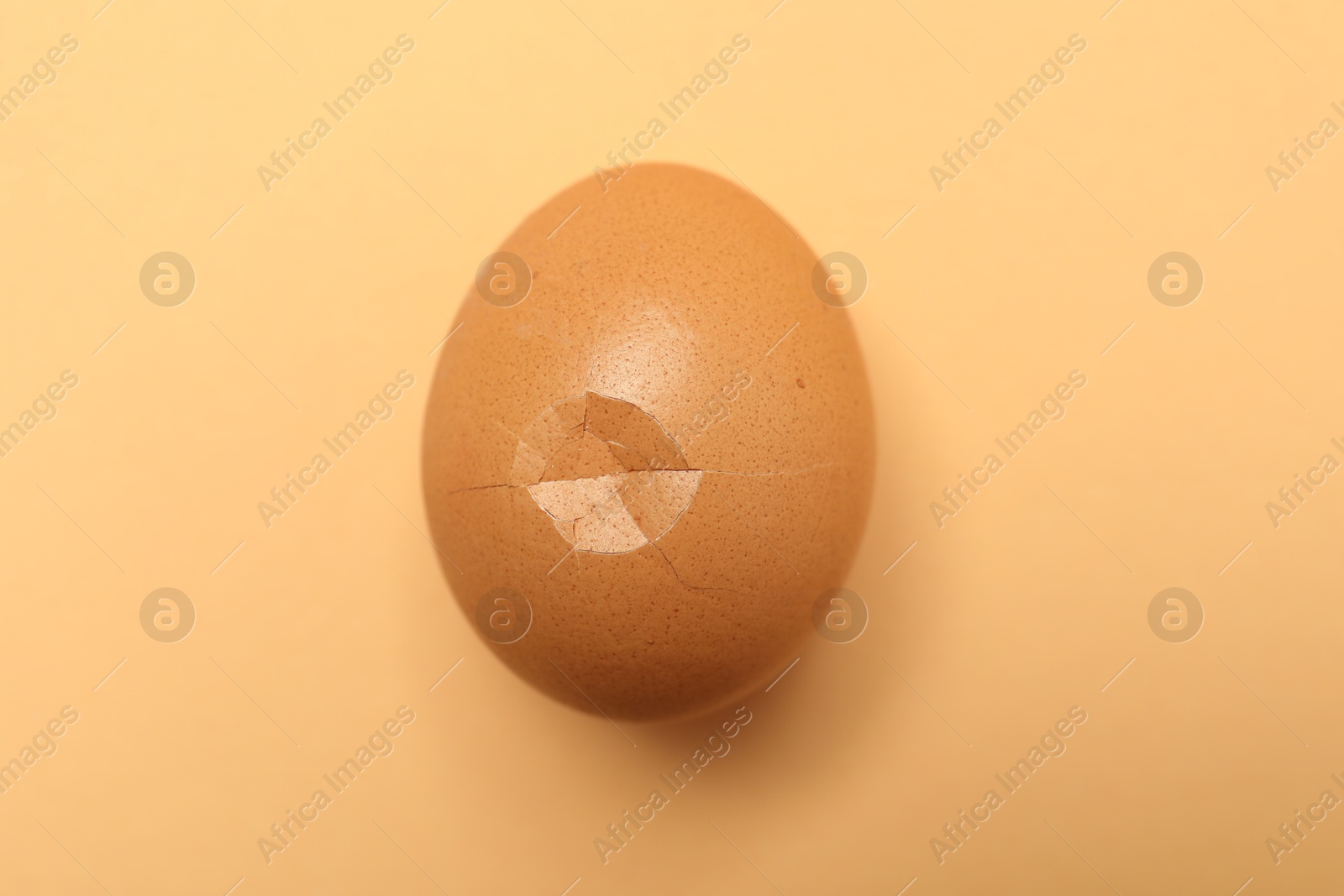 Photo of One egg with cracked shell on beige background, top view