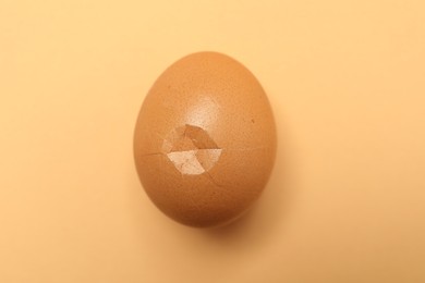 One egg with cracked shell on beige background, top view