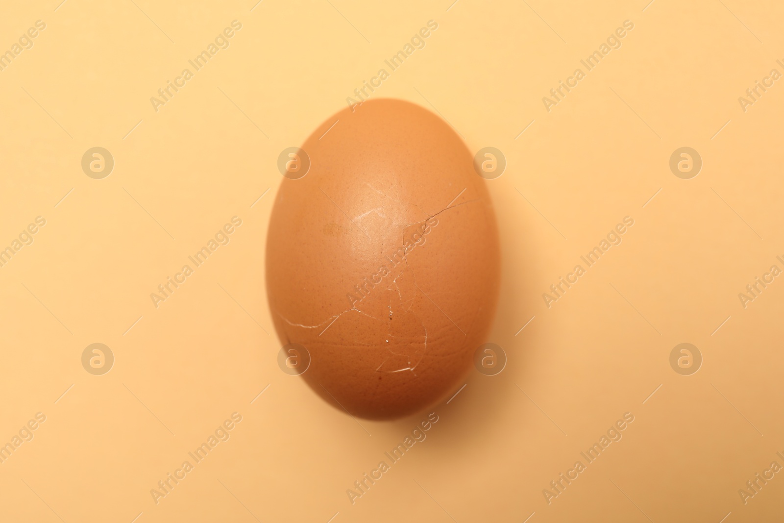 Photo of One egg with cracked shell on beige background, top view