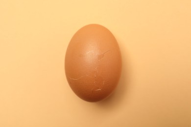 Photo of One egg with cracked shell on beige background, top view