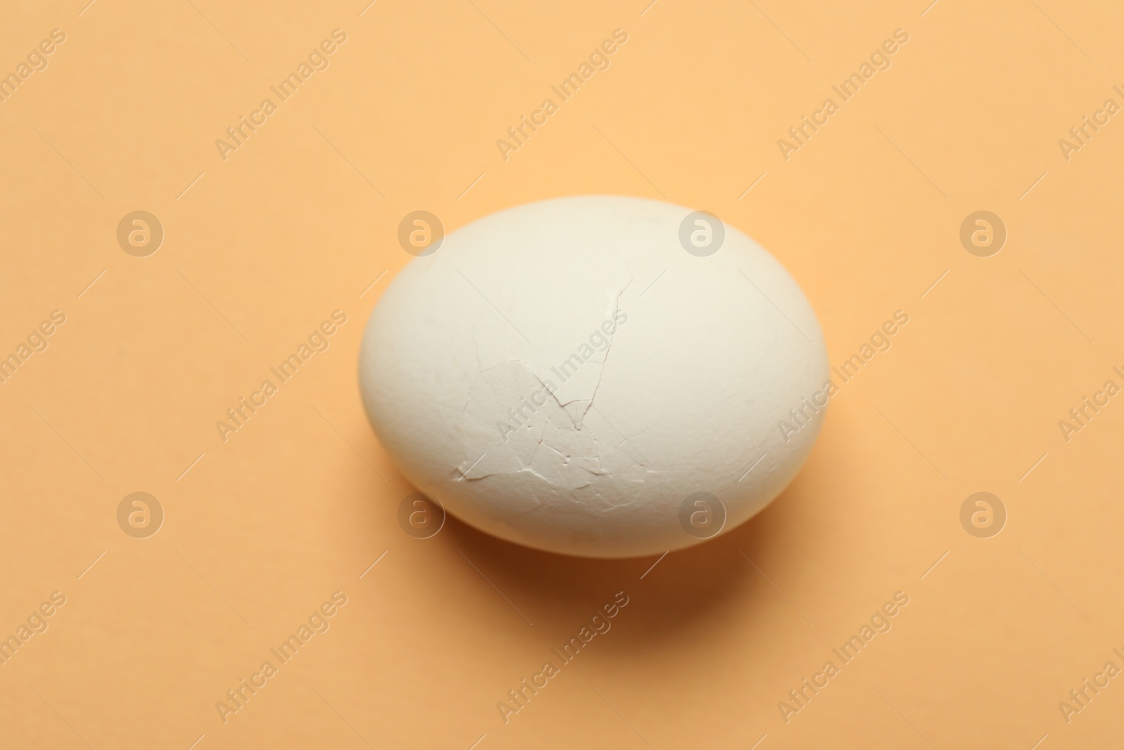 Photo of One egg with cracked shell on beige background, closeup