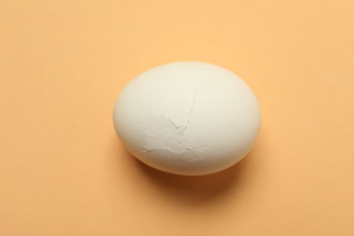 One egg with cracked shell on beige background, closeup