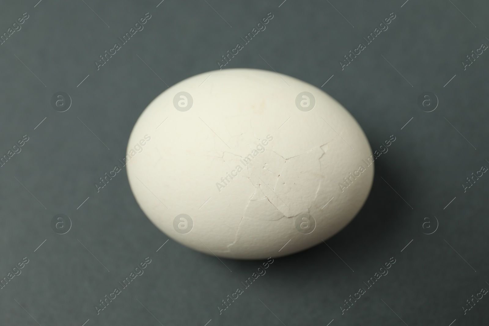 Photo of One egg with cracked shell on grey background, closeup