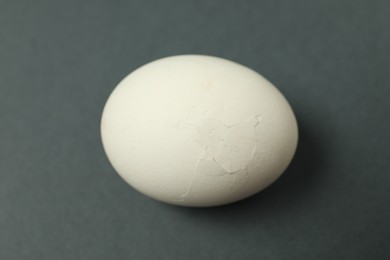 Photo of One egg with cracked shell on grey background, closeup