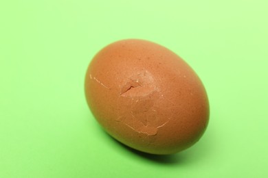 One egg with cracked shell on green background, closeup