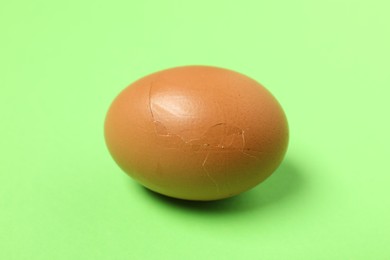 Photo of One egg with cracked shell on green background, closeup