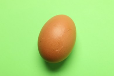 One egg with cracked shell on green background, above view