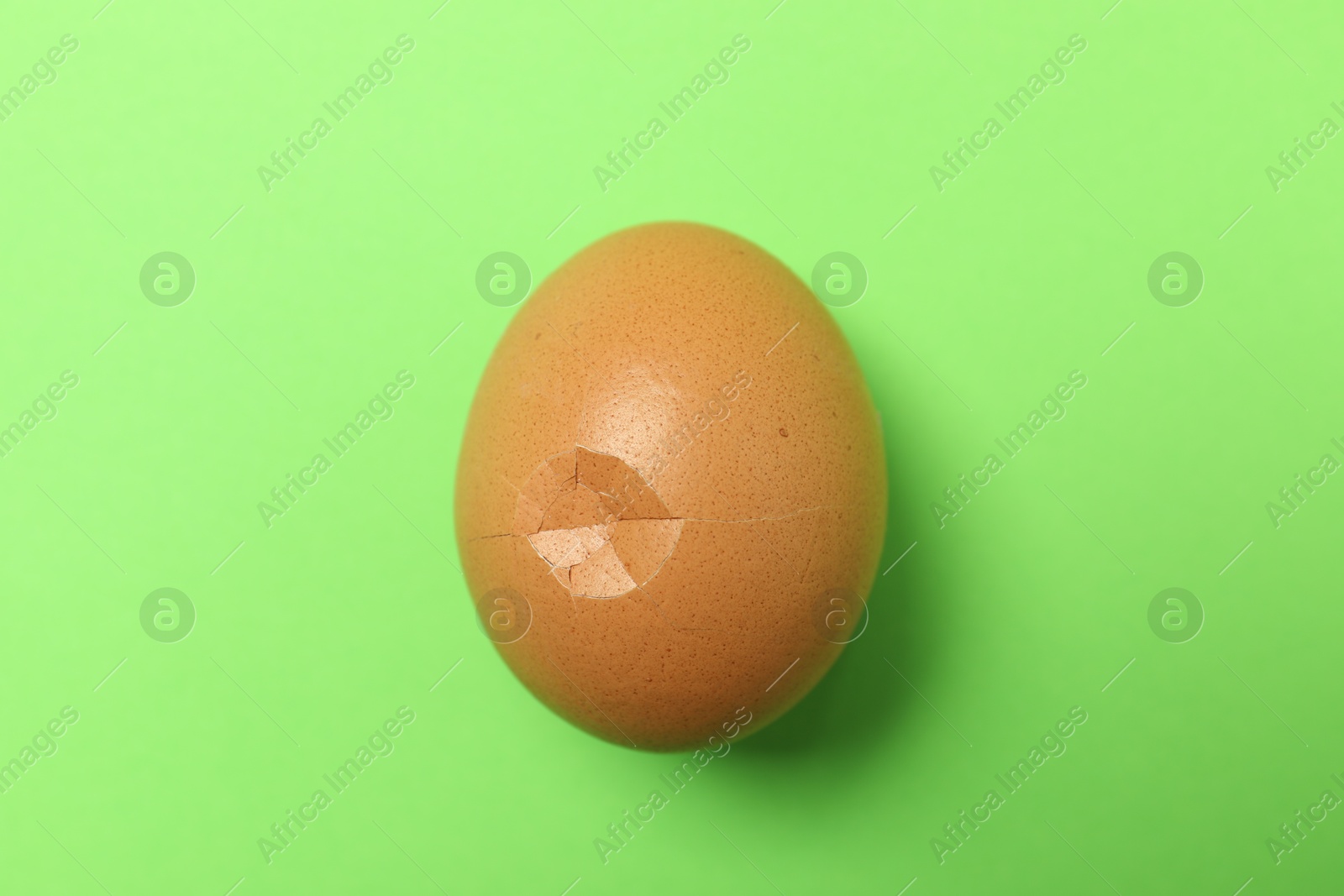 Photo of One egg with cracked shell on green background, top view