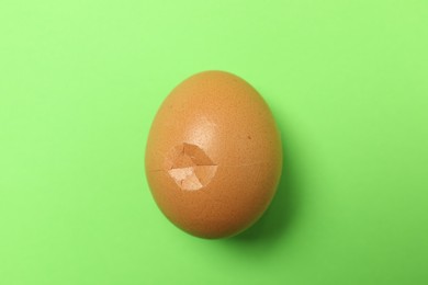 One egg with cracked shell on green background, top view