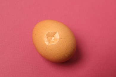 One egg with cracked shell on pink background, closeup