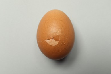 Photo of One egg with cracked shell on light grey background, closeup