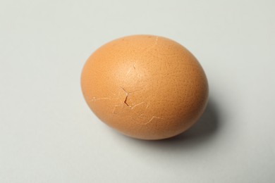 One egg with cracked shell on light grey background, closeup