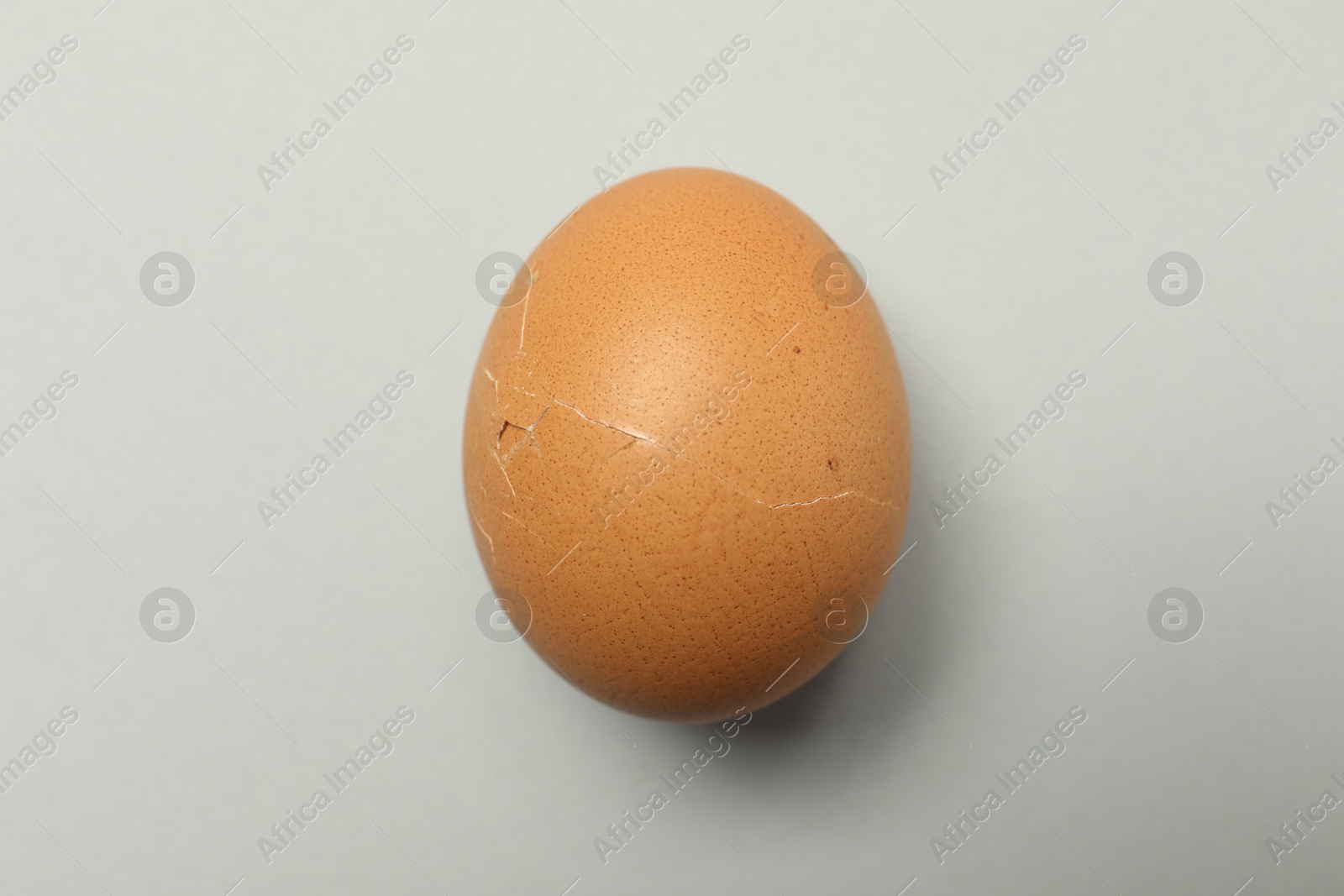 Photo of One egg with cracked shell on light grey background, closeup