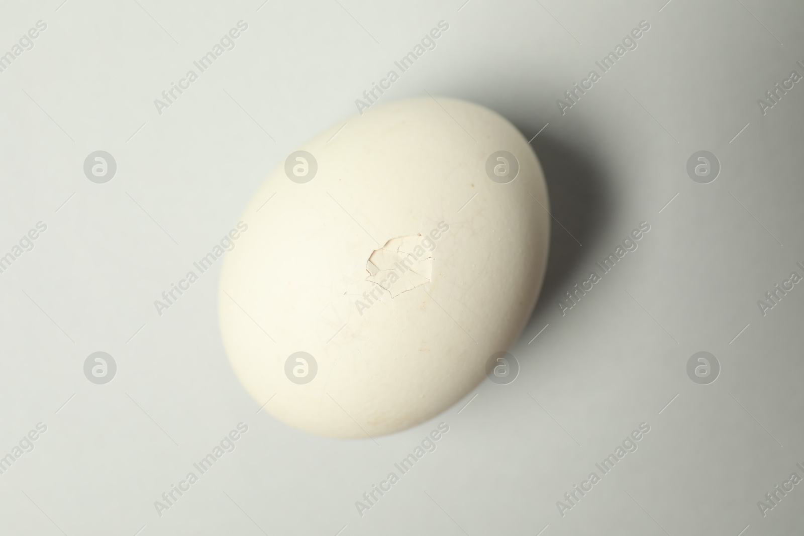 Photo of One egg with cracked shell on light grey background, top view