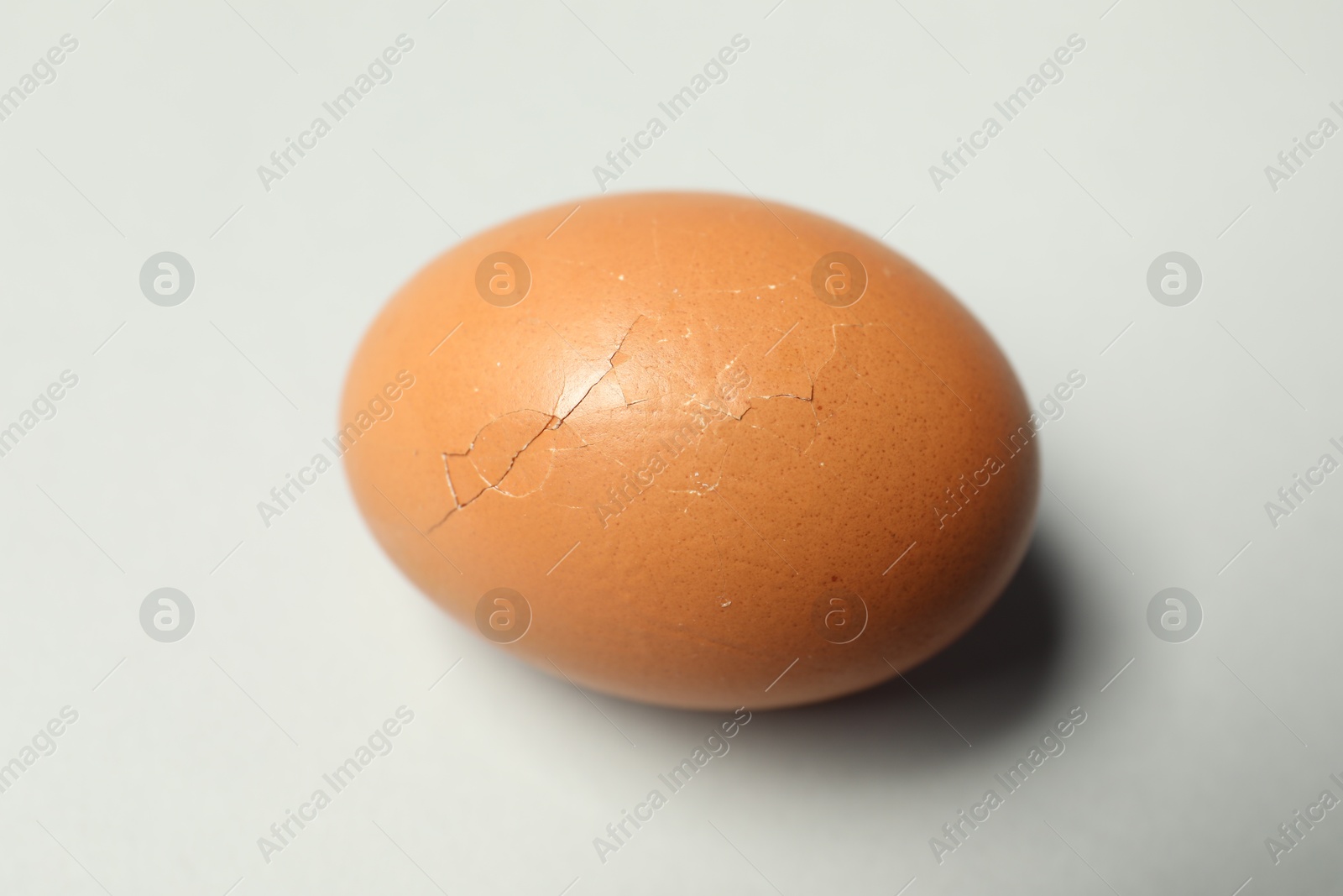 Photo of One egg with cracked shell on light grey background, closeup