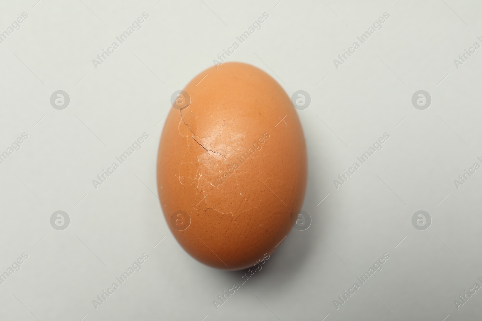 Photo of One egg with cracked shell on light grey background, top view