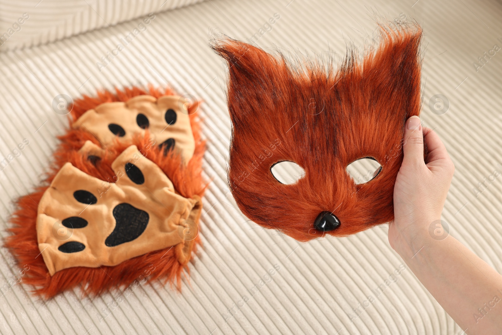 Photo of Quadrobics. Woman holding furry fox mask near sofa with gloves, closeup