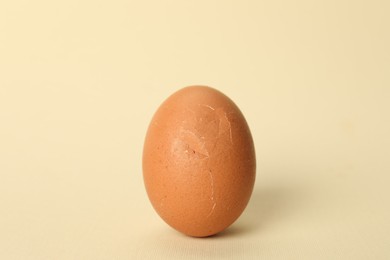 Photo of One egg with cracked shell on beige background, closeup