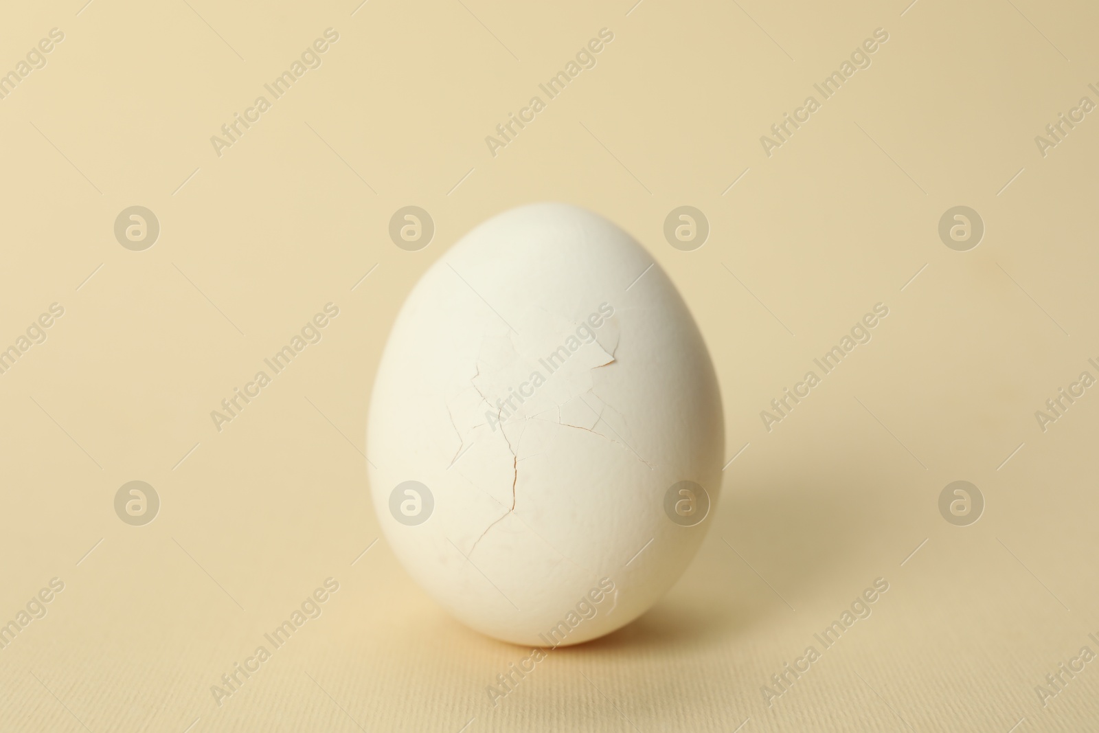 Photo of One egg with cracked shell on beige background, closeup