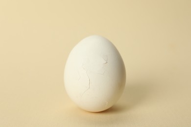 One egg with cracked shell on beige background, closeup