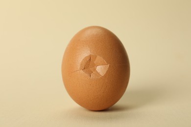 Photo of One egg with cracked shell on beige background, closeup