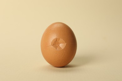 Photo of One egg with cracked shell on beige background, closeup