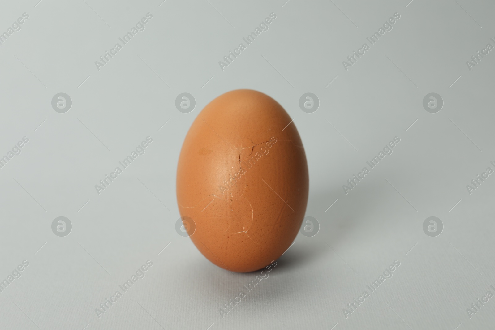 Photo of One egg with cracked shell on grey background, closeup