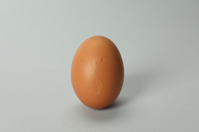 Photo of One egg with cracked shell on grey background, closeup