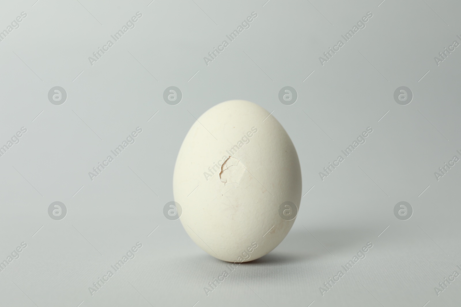 Photo of One egg with cracked shell on grey background, closeup