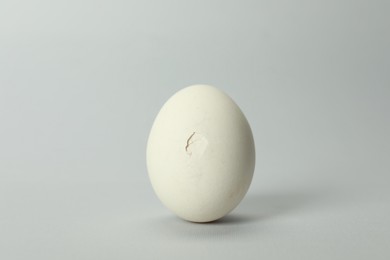 One egg with cracked shell on grey background, closeup