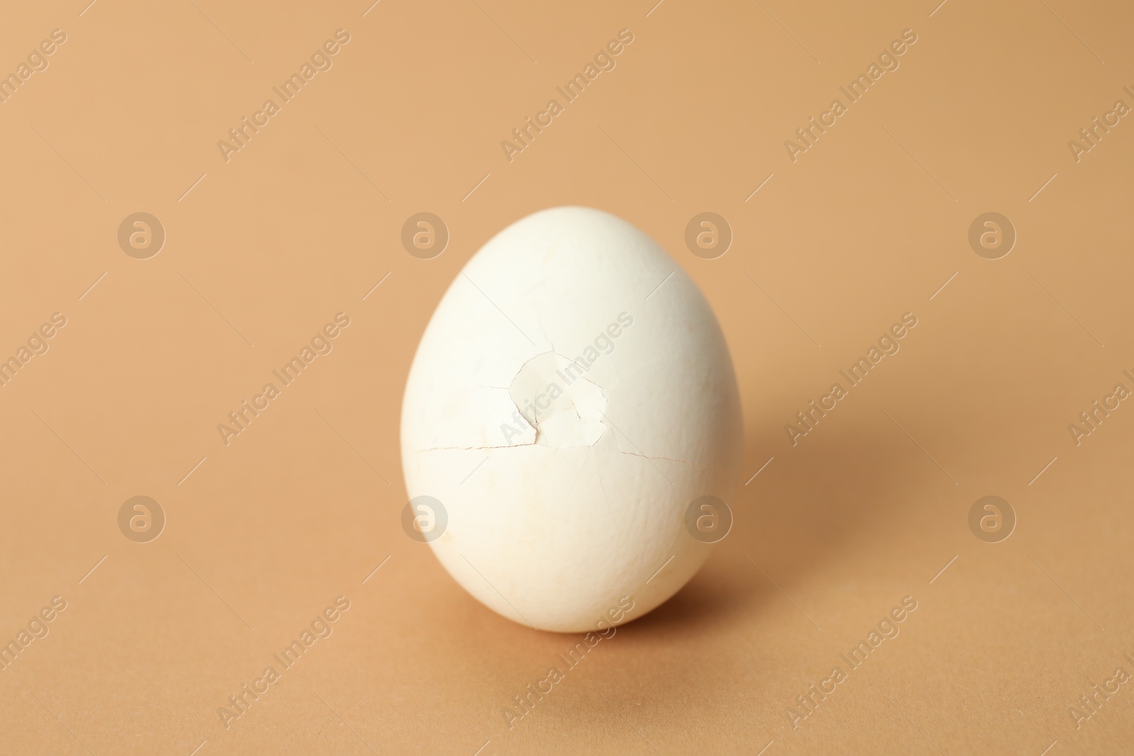 Photo of One egg with cracked shell on beige background, closeup