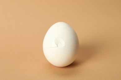 One egg with cracked shell on beige background, closeup