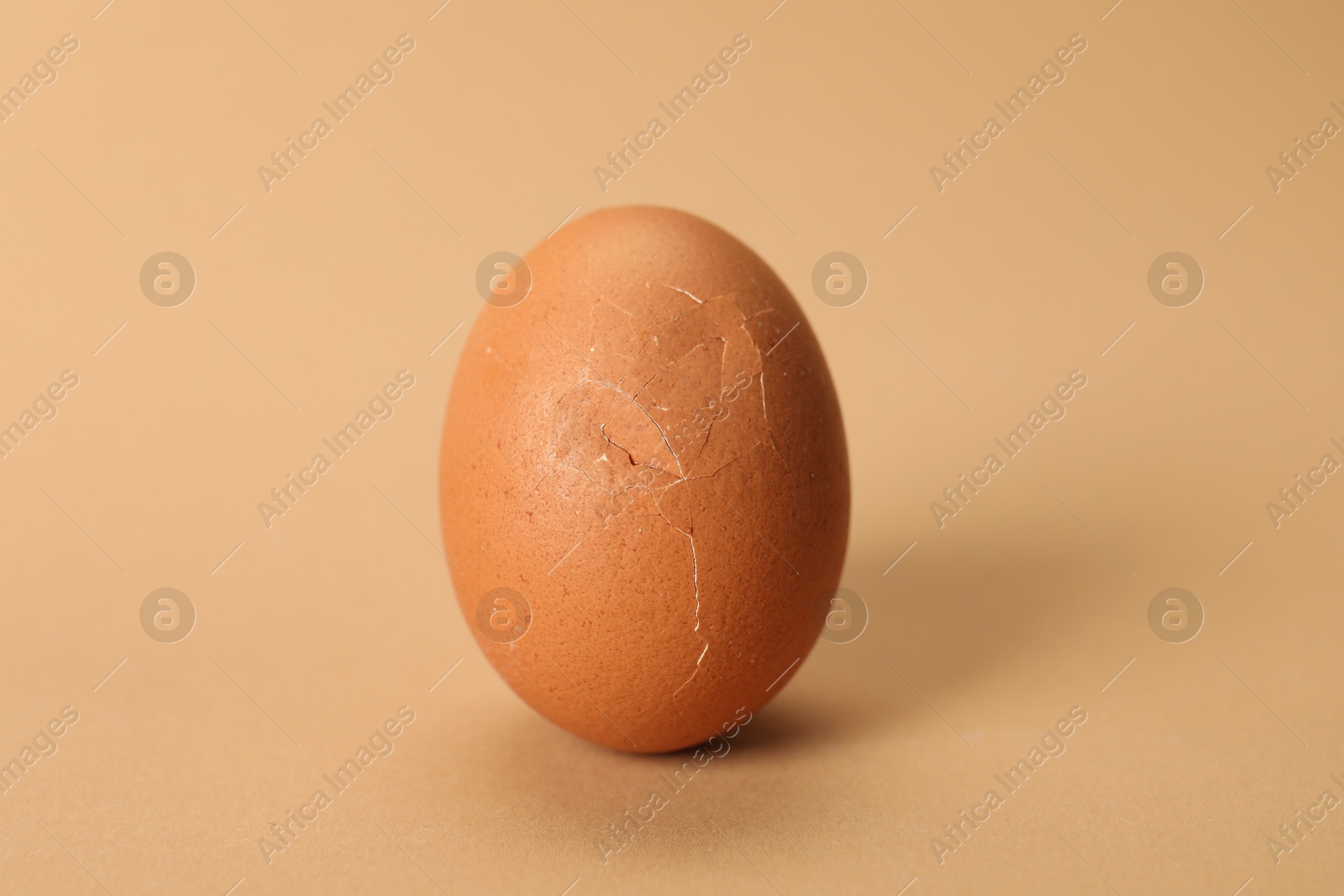 Photo of One egg with cracked shell on beige background, closeup