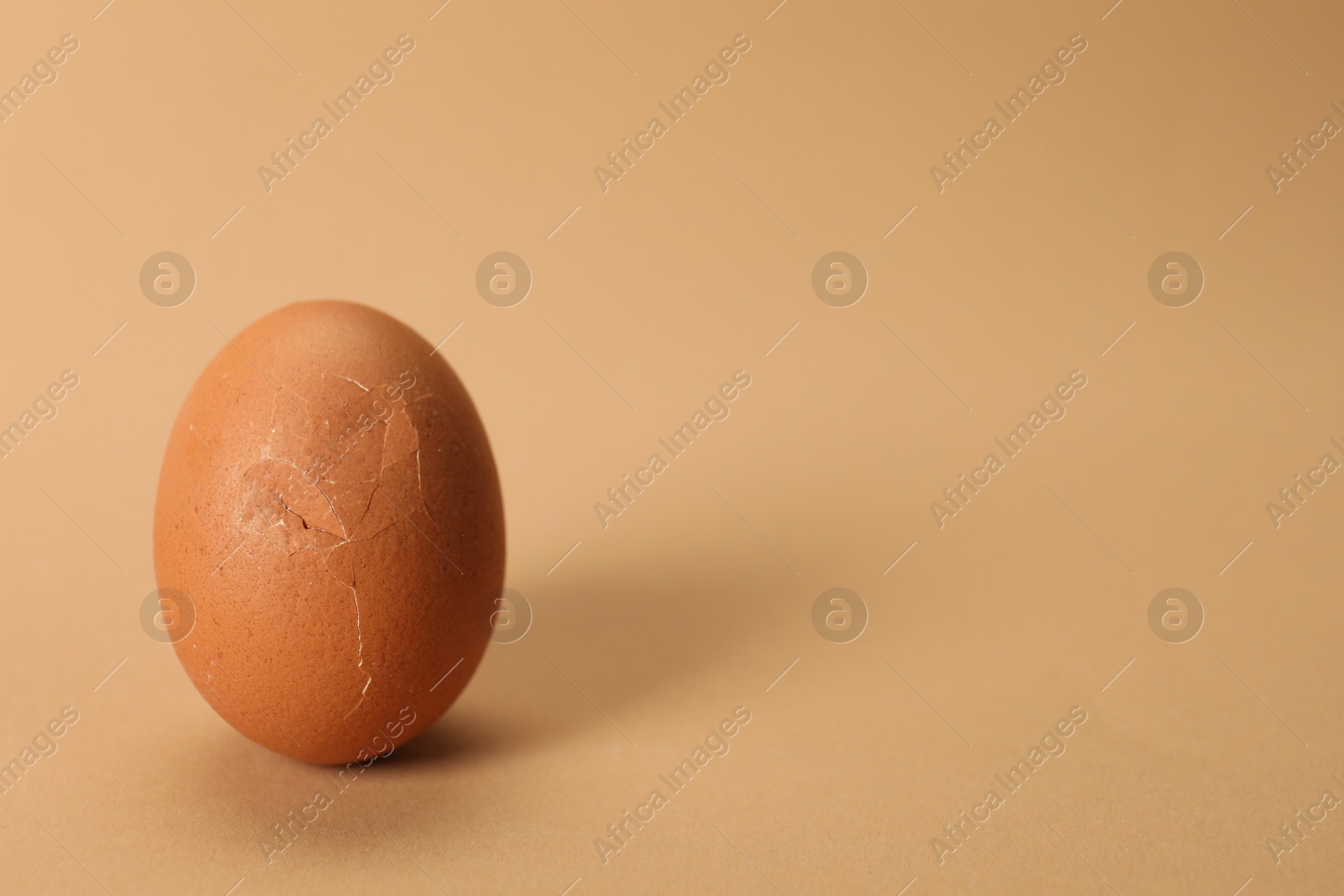 Photo of One egg with cracked shell on beige background, closeup. Space for text