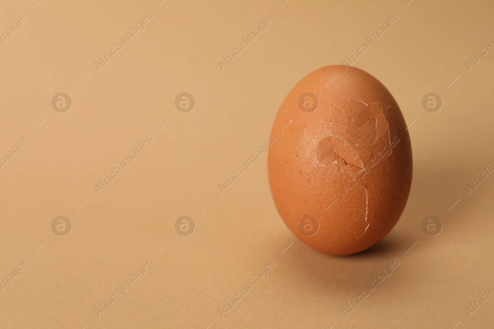 Photo of One egg with cracked shell on beige background, closeup. Space for text