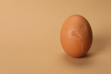 One egg with cracked shell on beige background, closeup. Space for text