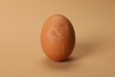 Photo of One egg with cracked shell on beige background, closeup