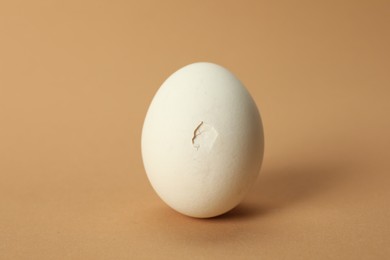 Photo of One egg with cracked shell on beige background, closeup