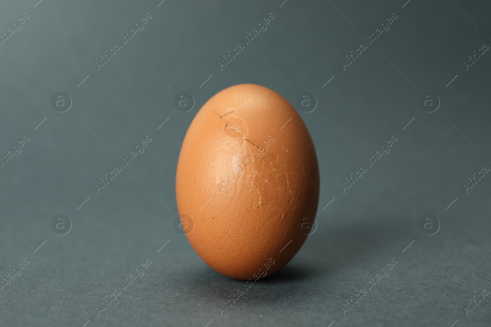 Photo of One egg with cracked shell on grey background, closeup