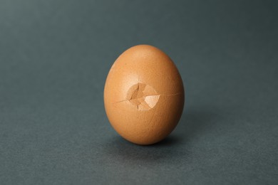 Photo of One egg with cracked shell on grey background, closeup