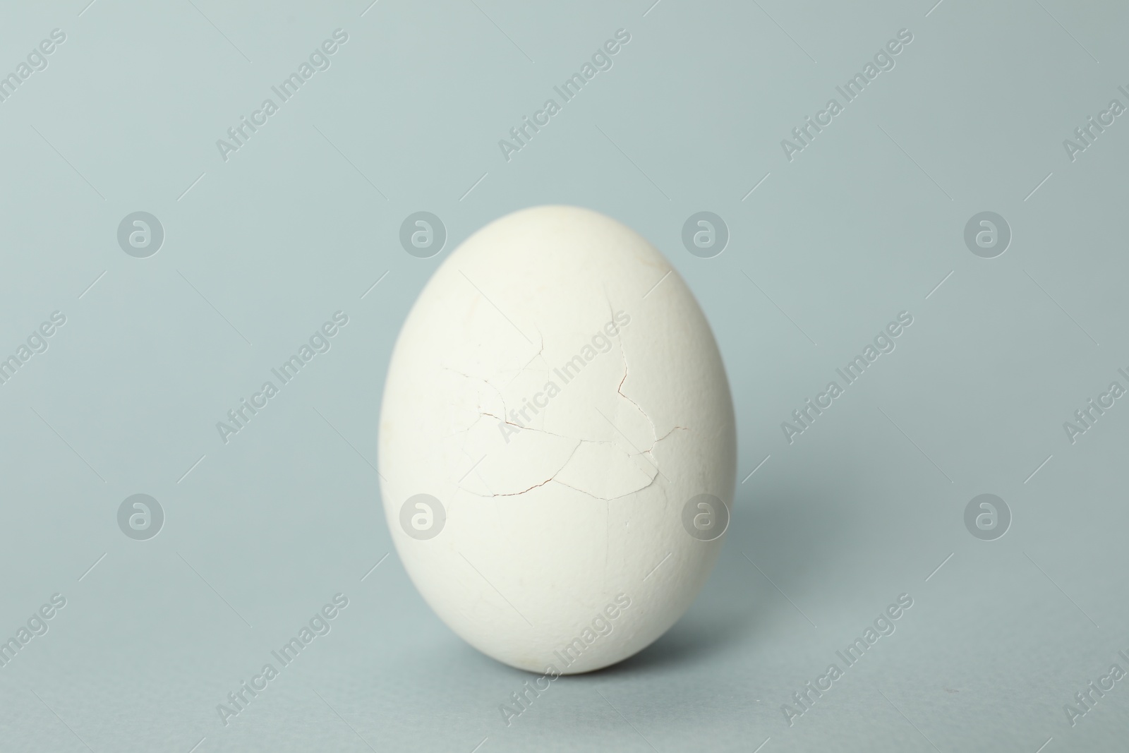 Photo of One egg with cracked shell on light grey background, closeup